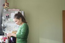 Vista laterale della donna media adulta in cucina facendo una tazza di tè, guardando in basso — Foto stock