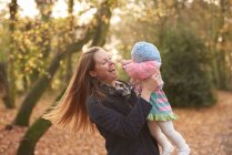 Mid adult woman swinging baby daughter in autumn park — Stock Photo