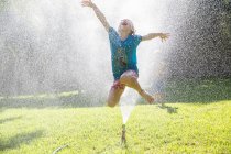 Mädchen springt über Sprinkleranlage im Garten — Stockfoto