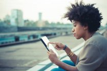 Young woman using touchscreen on digital tablet on city rooftop — Stock Photo