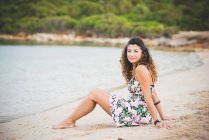 Frau sitzt am Strand und schaut in Kamera — Stockfoto