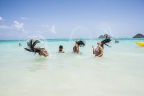Вид сбоку на молодых женщин, выбрасывающих длинные мокрые волосы обратно в море на пляже Ланикай, Оаху, Гавайи, США — стоковое фото