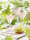 Trois verres de cocktails de martini rose aux olives vertes — Photo de stock