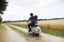 Rear view of mature man and daughter riding motor scooter along dirt track — Stock Photo