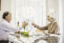 Coppia di anziani seduti insieme a tavola, tenendo bicchieri di vino, facendo toast — Foto stock