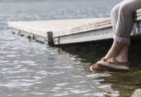 Legs of young man dangling from pier — Stock Photo