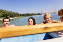 Freunde mit nassen Haaren im See halten sich am Boot fest und schauen in die Kamera, Schondorf, Ammersee, Bayern, Deutschland — Stockfoto