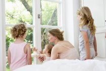 Mãe e três filhas olhando pela janela — Fotografia de Stock