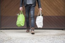 Teenage boy carrying reusable shopping bags full of empty bottles for recycling — Stock Photo