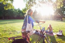 Молода жінка прибуває на велосипеді на вечірку парку заходу сонця — стокове фото