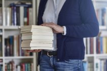 Schnappschuss von Frau, die Bücherstapel aus Bücherregalen trägt — Stockfoto