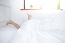 Ноги, що стирчать з ковдри на ліжку — стокове фото