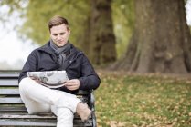 Young man reading newspaper on park bench — Stock Photo