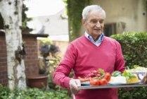 Старший чоловік несе лоток зі свіжої їжі та овочів — стокове фото