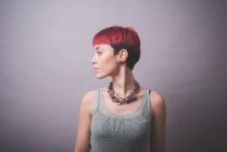 Studioporträt einer jungen Frau mit kurzen rosafarbenen Haaren, die über ihre Schulter blickt — Stockfoto