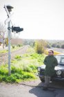 Середній дорослий чоловік спирається на старовинний автомобіль на залізничному переході — стокове фото