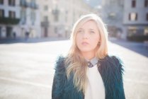 Portrait of funky young woman wearing furry jacket in town square — Stock Photo