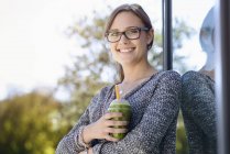 Portrait of young woman with takeaway coffee leaning against park building — Stock Photo