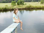 Chica adolescente sentada en el trampolín sobre el lago - foto de stock