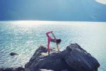Mitte erwachsene Frau, balancierend auf Felsen am See, in Yogaposition — Stockfoto