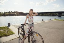 Retrato de uma jovem mulher com bicicleta à beira-rio, Ilha do Danúbio, Viena, Áustria — Fotografia de Stock
