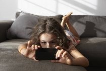 Girl lying on living room sofa looking at smartphone — Stock Photo