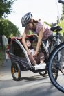 Mother fastening daughter seatbelt in bicycle trailer — Stock Photo