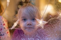 Petite fille regardant par la fenêtre avec des décorations de Noël — Photo de stock