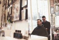Imagem espelhada do barbeiro que fixa a capa do cliente na barbearia — Fotografia de Stock