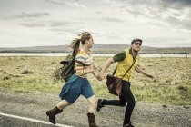 Retro style couple running hand in hand on roadside, Cody, Wyoming, USA — Stock Photo