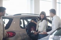 Mid adult couple with baby girl trying out baby seat in car dealership — Stock Photo