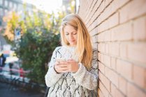 Frau schreibt SMS auf Smartphone, gegen Ziegelmauer — Stockfoto