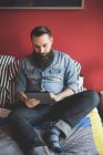 Молодой бородатый человек с помощью цифровой таблетки на кровати — стоковое фото