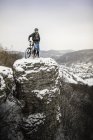 Молодий чоловічий гірський велосипедист на вершині снігового покриття скельного утворення — стокове фото