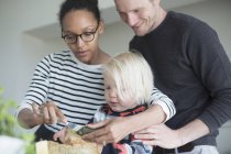 Boy preparing food in kitchen with parents at home — Stock Photo
