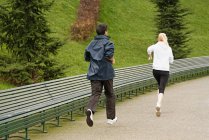 Man and woman running along pathway, rear view — Stock Photo