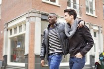 Two young men strolling down the street with arms around each other — Stock Photo