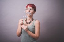 Portrait studio de jeune femme tenant lunettes et moustache devant le visage — Photo de stock