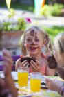 Mädchen essen Schokoladenkuchen, Gesicht mit Zuckerguss bedeckt — Stockfoto