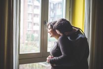 Casal em pé à janela, abraçando — Fotografia de Stock