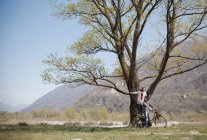 Молодая женщина, стоящая на велосипеде позади парня в поле — стоковое фото