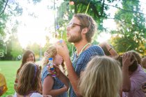 Молодий чоловік дме бульбашки на груповій вечірці в парку на заході сонця — стокове фото