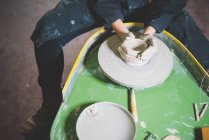 Vue grand angle de la jeune femme, la taille vers le bas, assis à la roue de poterie faisant pot d'argile — Photo de stock