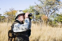 Homme âgé regardant à travers les jumelles sur safari, parc national de Kafue, Zambie — Photo de stock