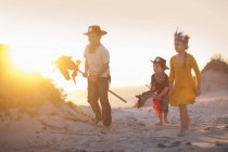 Tres niños vestidos como nativos americanos y vaqueros en dunas de arena - foto de stock