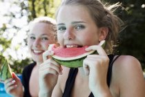 Дві дівчинки-підлітки їдять скибочки кавуна в саду — стокове фото