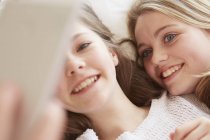 Close up of two girls lying on bed taking smartphone selfie — Stock Photo