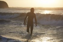 Silhouette de jeune surfeur homme portant une planche de surf en mer, Devon, Angleterre, Royaume-Uni — Photo de stock
