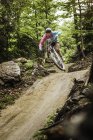 Young female mountain biker jumping mid air in forest — Stock Photo