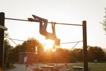 Silhouetted young woman upside down on playground climbing frame at sunset — Stock Photo